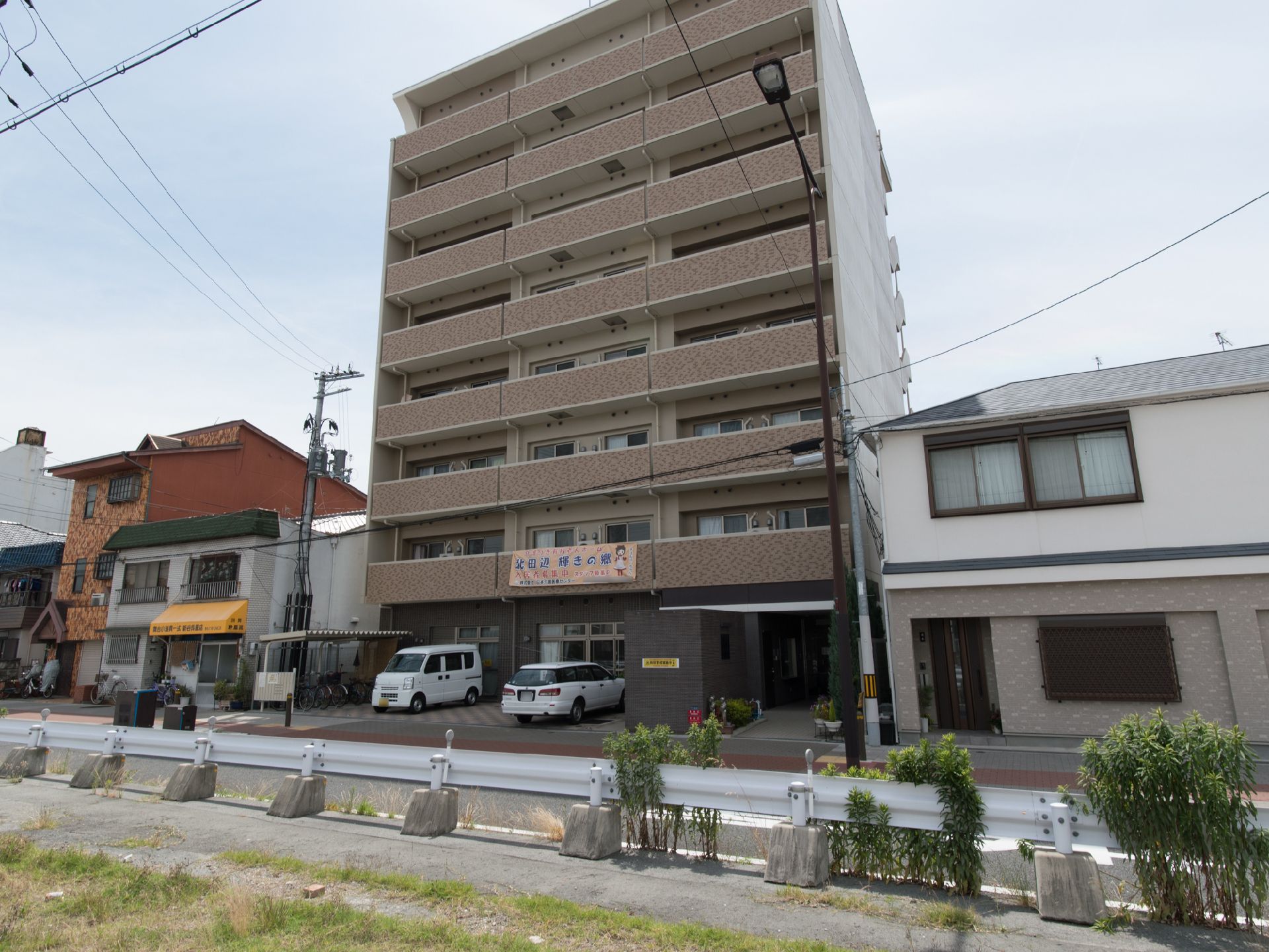 住宅街の一角にある施設で、全体的に外観が茶色である。玄関前に駐車場がある。プランターが置いてあるほか、木々も植えてある。