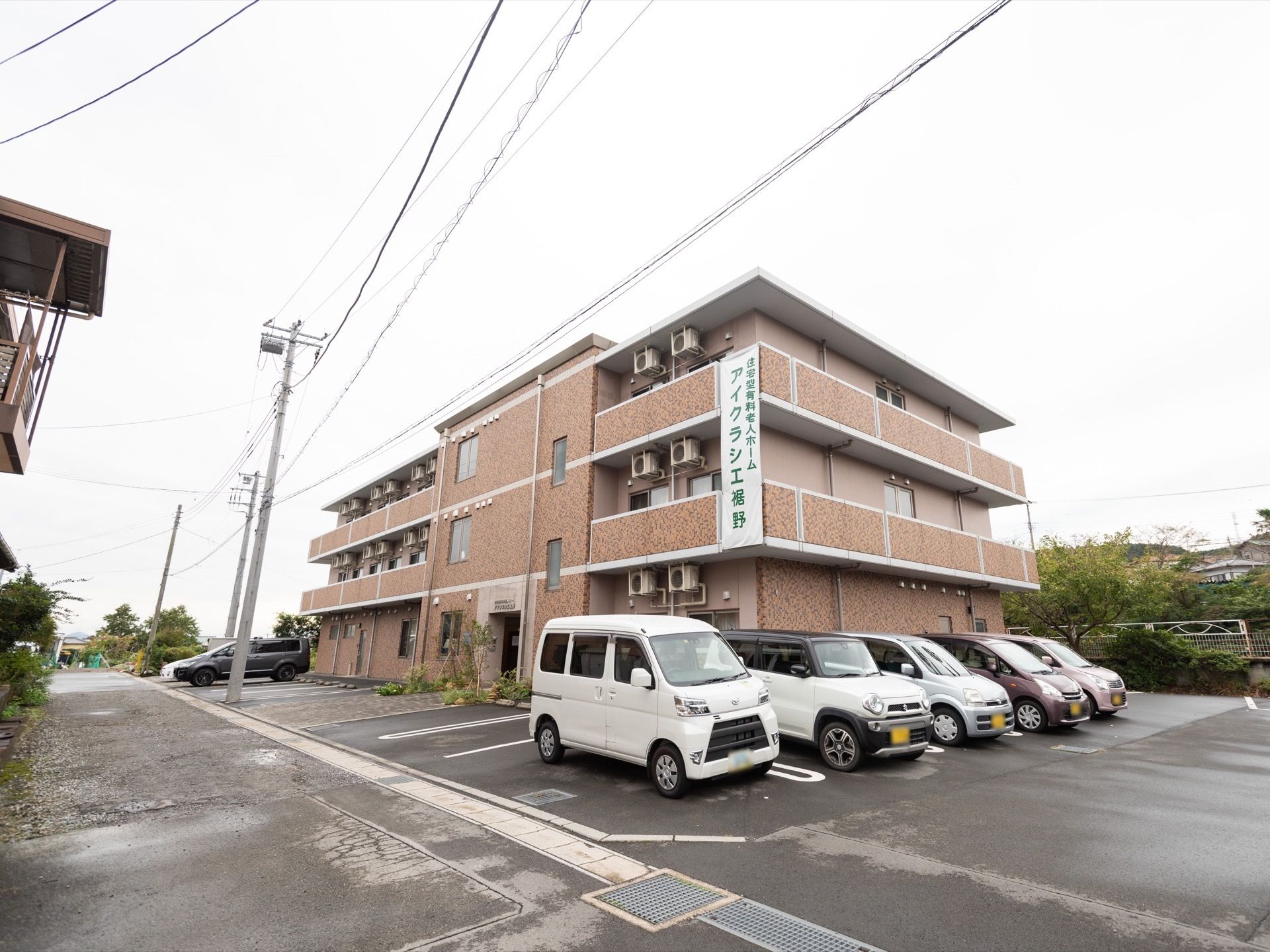 茶色を基調として、所々の縁どりに白色が使われている外壁の３階建ての施設である。２面が道路に面している敷地である。