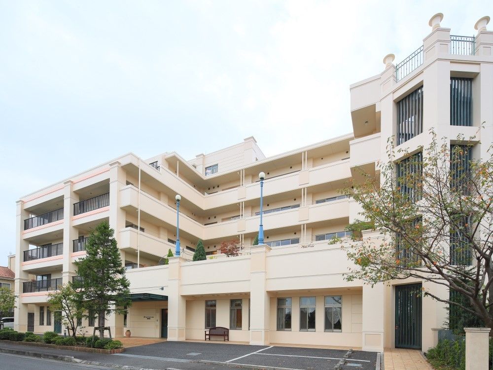 閑静な住宅街の中にある建物。広い道路に面しており、敷地内にはアスファルトで舗装された駐車スペースが設けられている。