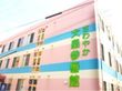 明るい緑色の文字で施設名が書かれた建物。外観は薄いピンクをメインに、水色、白のボーダー模様が施されたさわやかな色合いである。
