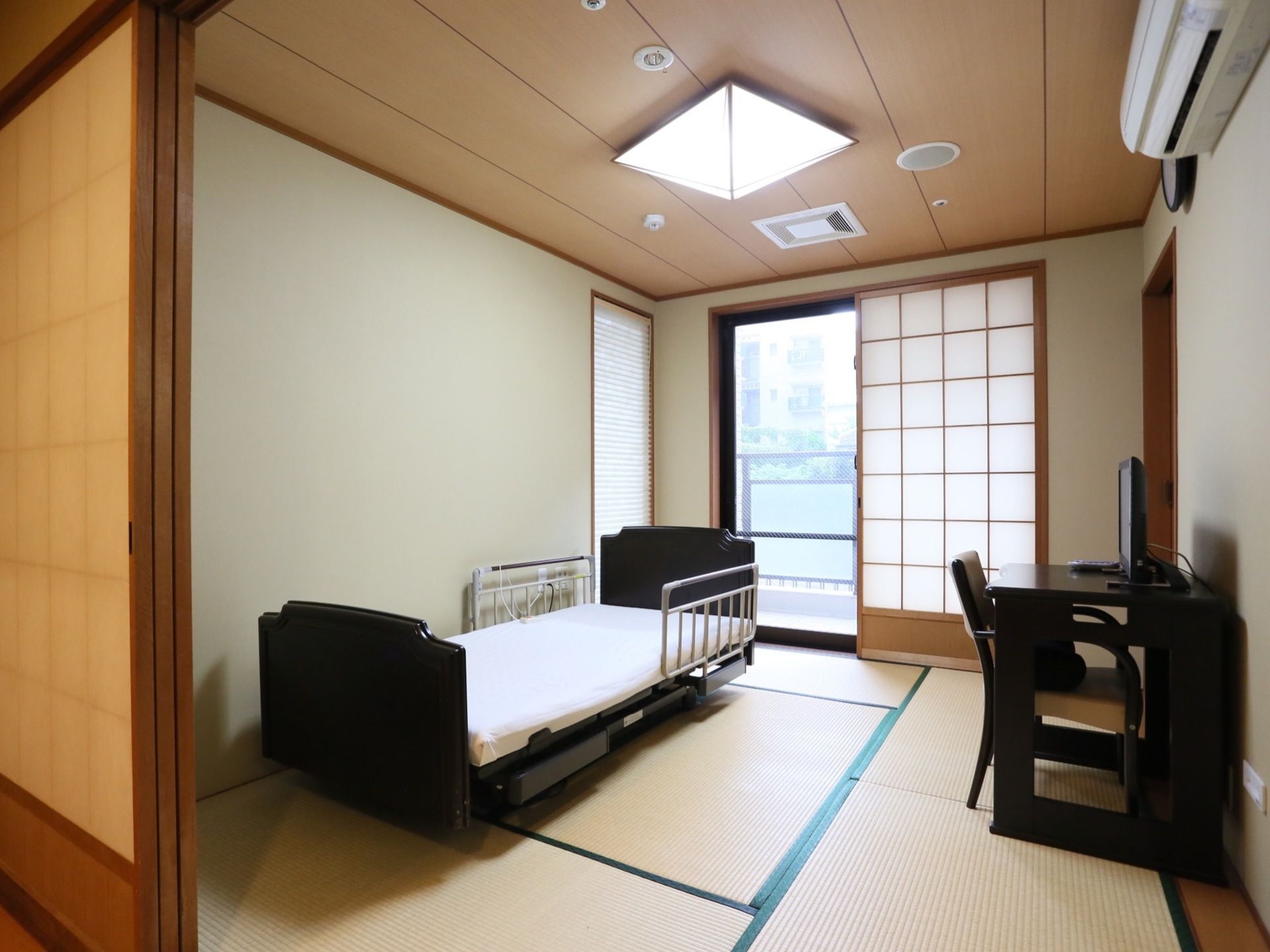 畳を敷設した居室である。壁際に介護用ベッドを配置している。テーブルと椅子を備え、その上にテレビを置いている。