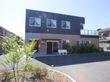 落ち着いた色調の外観で鉄骨造り2階建てになっている。玄関前には白いベンチがあり、その脇には木々も植えられている。
