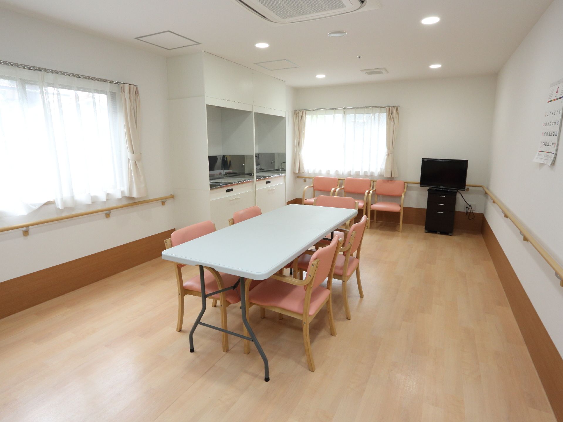 白い壁で明るくピンク色のイスが印象的な部屋で、入居者同士で会話を楽しんだり、カラオケを楽しむことができる。
