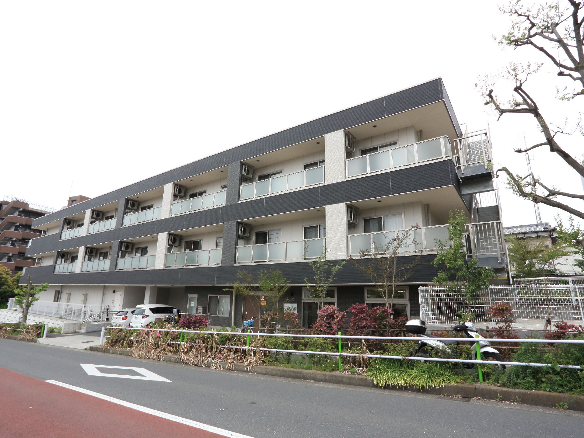 3階建ての建物は黒が基調となっていて鉄骨造になっている。各部屋のベランダ側が道路に面していて、エアコンの室外機が見えている。