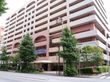 建物正面前には片側2車線の道路と歩道がある。歩道と建物の間に低木の植栽帯があり、所々に高木が配置されている。