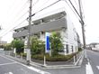 白と黒を基調とした３階建ての建物である。建物の周囲には植物が多く植えられていて、木の横に青い看板がある。