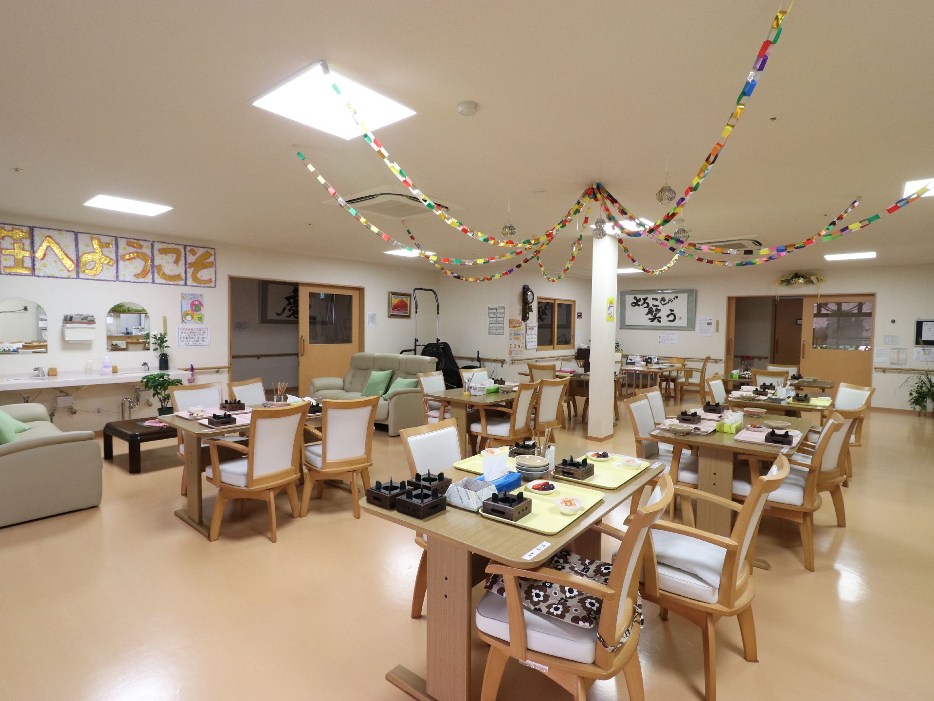 色とりどりの紙で作られた輪っか飾りが天井にある。沢山置かれたテーブルと椅子、扉の近くにはソファーと机が置かれている。
