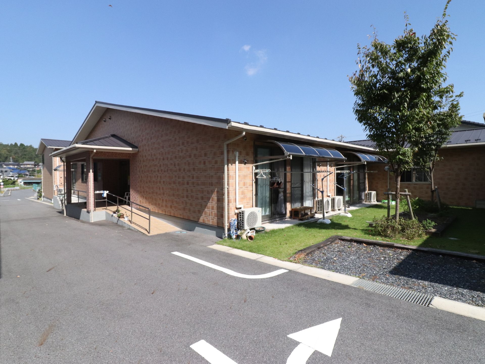 平屋のレンガ造り風な外装の建物。日当たりのよい芝生がある庭があり、洗濯ものを干すことが出来るようになっている。