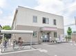 二階建てのツートンカラーの建物である。外に自転車置き場がある。出入り口の横にはベンチと自動販売機が置かれている。