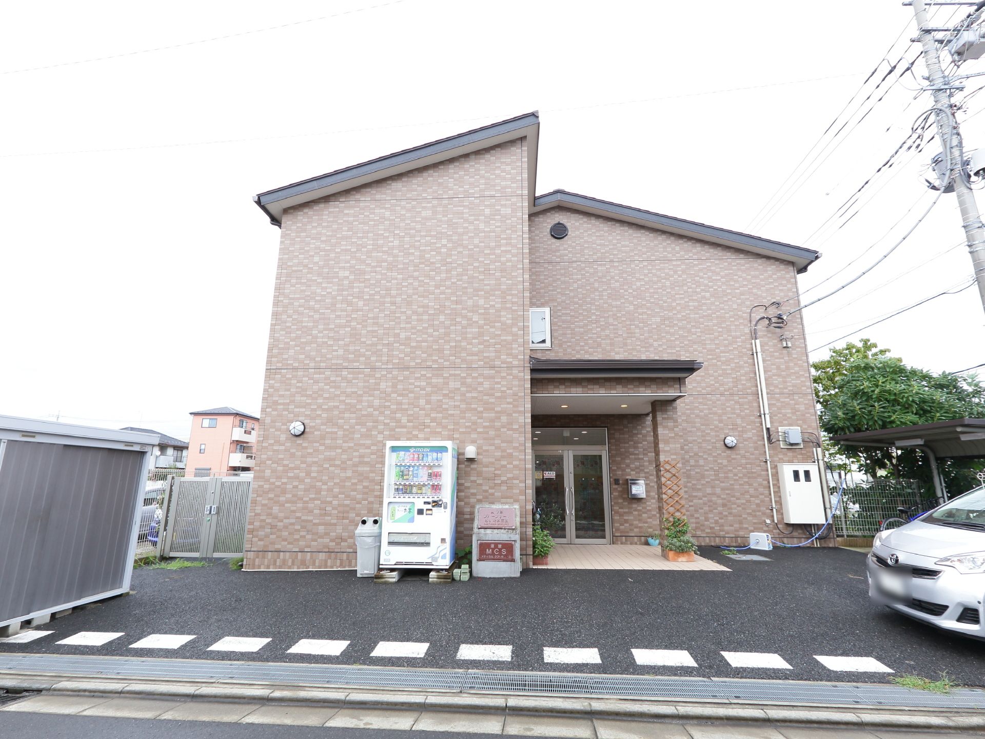 施設の玄関前には屋根の付いた自転車置き場が見られる。自動販売機も設置されている。車道から入り易いので便利である。