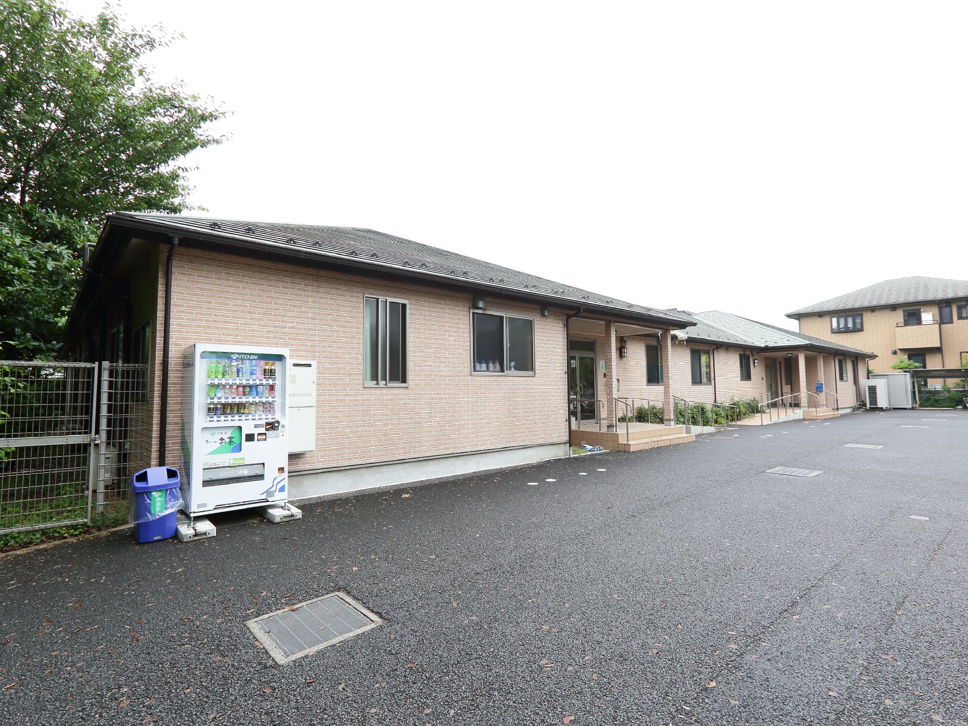 大きな平屋のホームの外観。たくさんの緑に囲まれ、恵まれた環境にある。建物の端には自動販売機が設置されている。