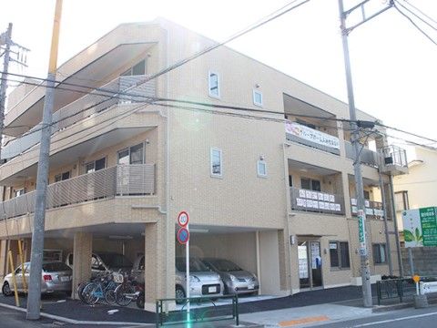 建物は３階建てで、１階部分には屋根付きの駐車スペースが設けられている。壁はベージュで２階と３階にはベランダがあり、掃き出し窓が付いている。