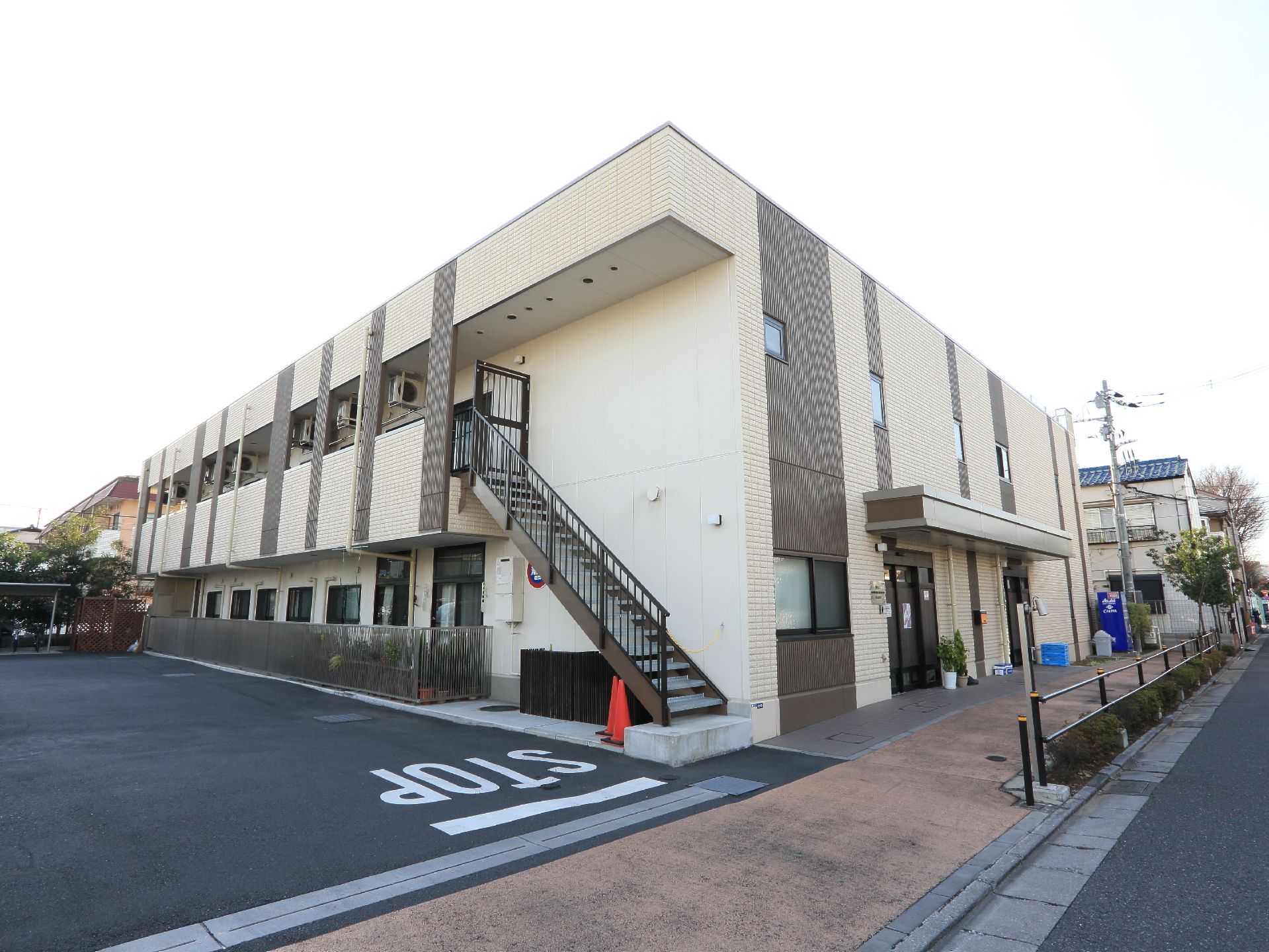 建物の外観。隣にはグループホームの広い駐車場がある。建物は茶色と落ち着いた白系のタイルで造られており、落ち着いた印象。
