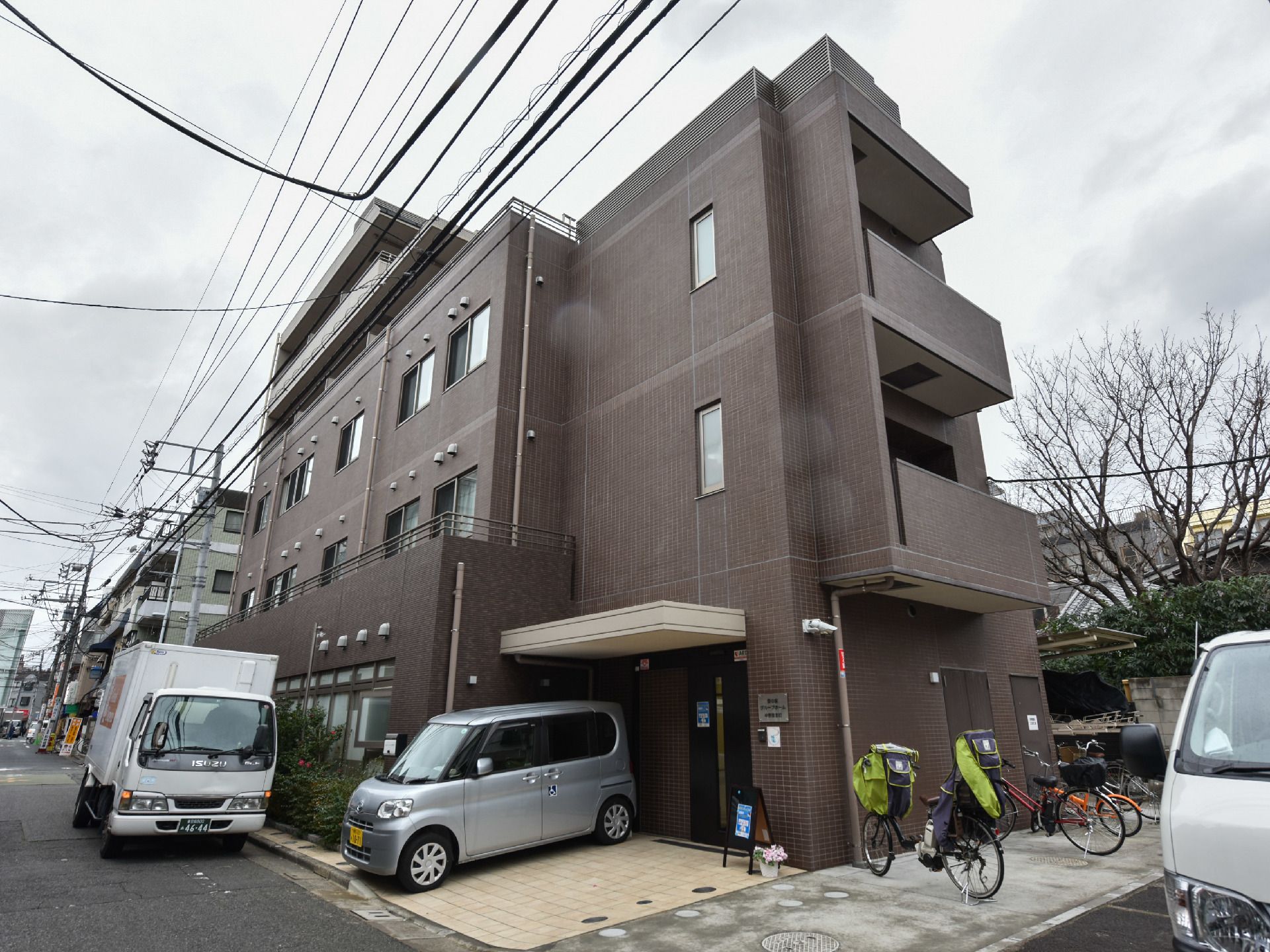愛の家グループホームの建物外観。入り口ドアの隣には車を1台駐車することができる。自転車置き場もある。