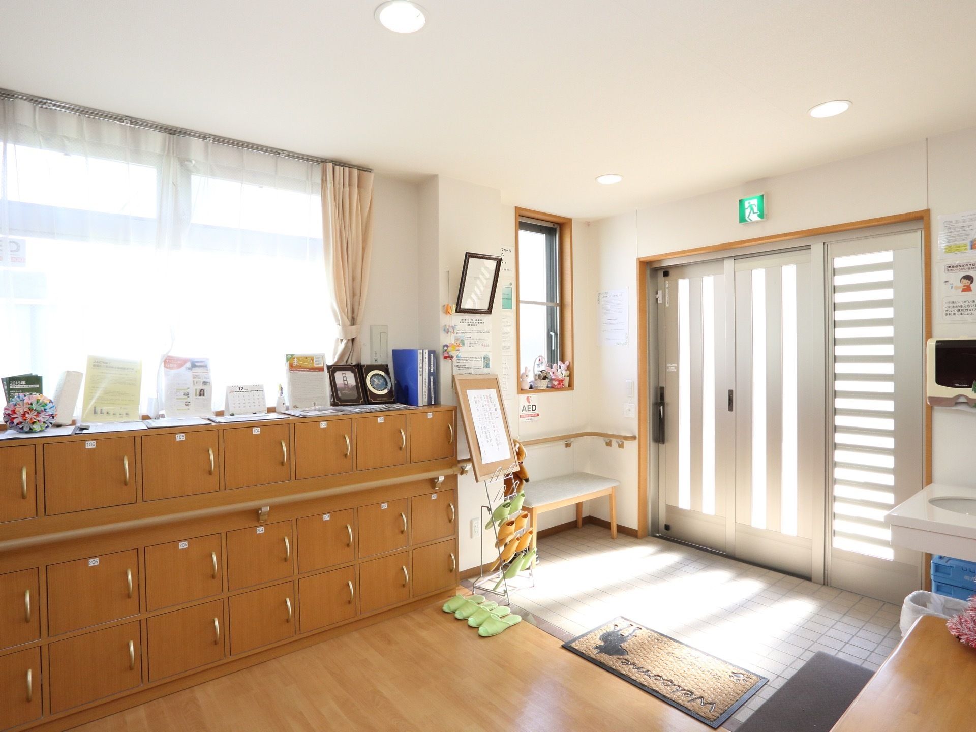 陽射しがたっぷり入る施設の入口である。各入居者様用の靴箱が設置されている。手すりやベンチが配備されている。