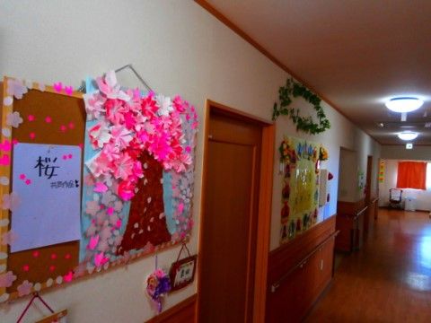 白い壁は腰から下が板張りで、手すりが付いている。上の方には掲示物が並んでおり、手前には折り紙で作られた桜のオブジェがある。