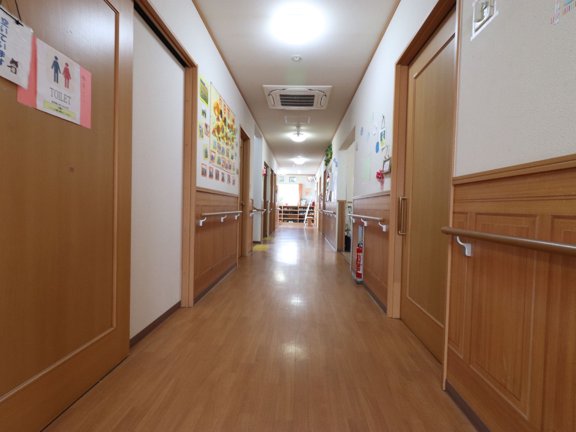 共用廊下の両側の壁には手摺が設置してある。その上には行事の際に撮影した記念写真が掲示してある。消火器が置かれている。