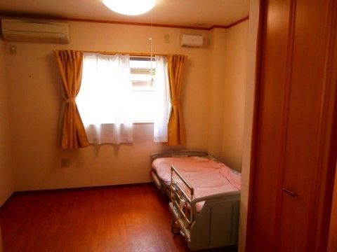 正面に腰高窓があり、天井近くにはエアコンが設置してある。エアコンと離れた壁際に頭を窓に向けてベッドが置かれている。