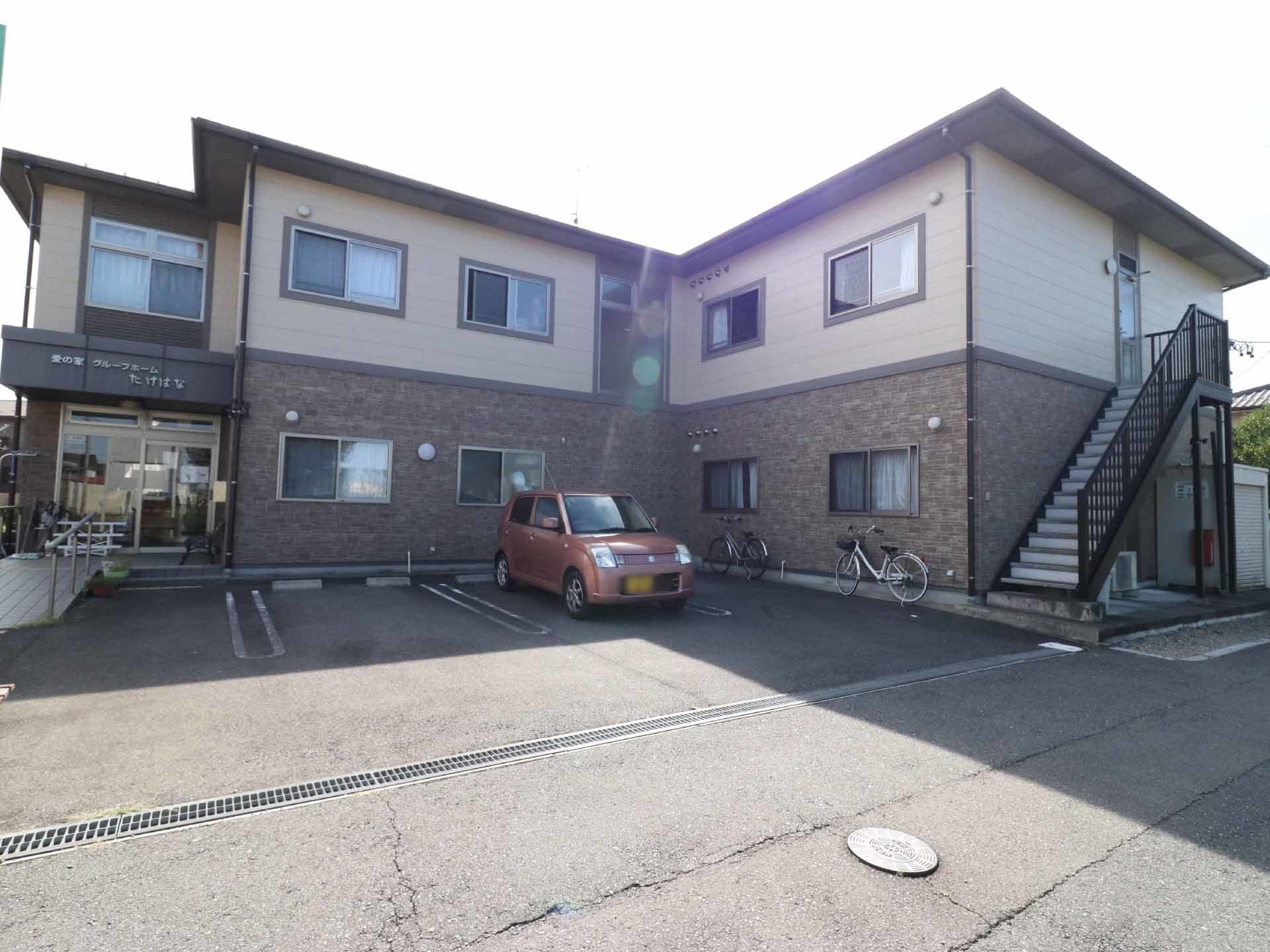 2階建ての施設は1階が茶色、2階がクリーム色の外壁である。エントランスから離れた位置に、外付けの階段が設けられている。