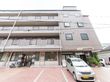 施設は4階建ての茶色い建物で、窓とフェンスのフレームは黒である。玄関がある右側部分は外開き窓が設置されている。