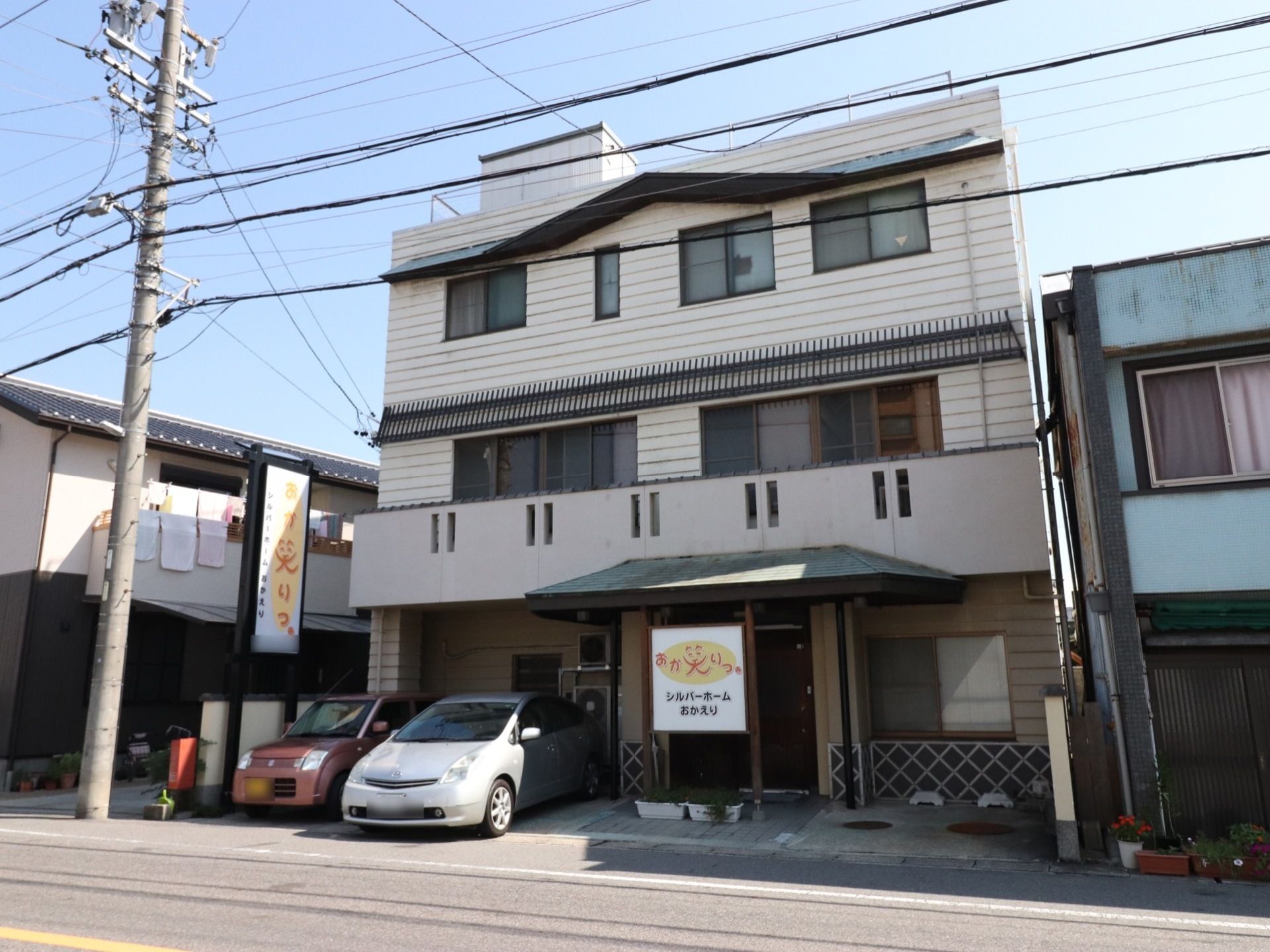 一戸建ての家を改造してできた老人施設である。玄関前と駐車場の横には、こちらの施設名が書かれた看板が掲げられている。屋上には物置がある。
