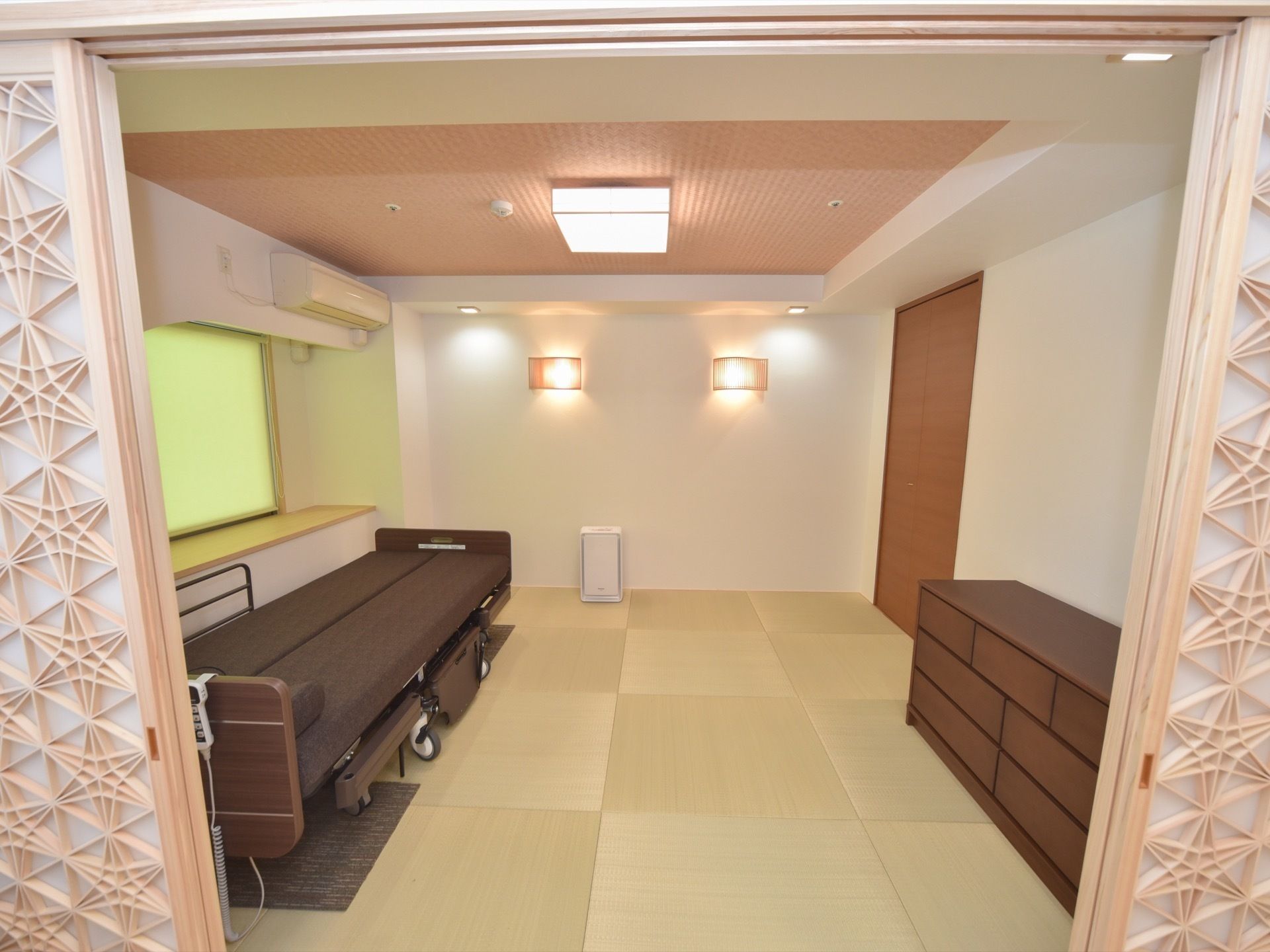 半畳の畳が市松模様のように敷き詰められた和室に、和ダンスや同じカラーのダークブラウンの介護ベッドが置かれている。