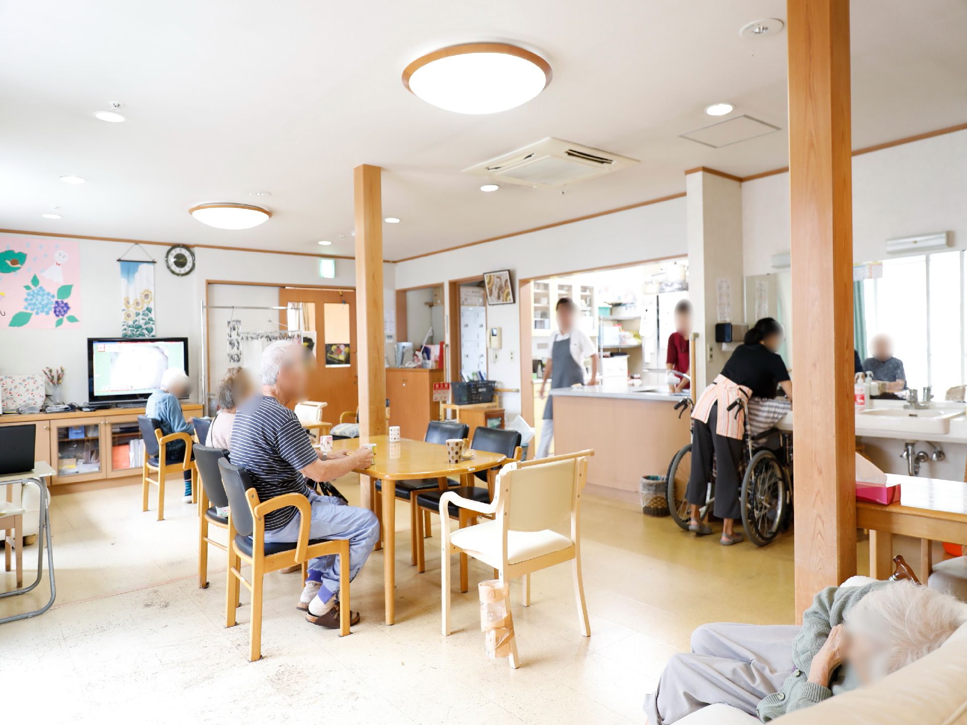 お茶の時間なのか、入居者が揃って、湯呑みを手にしている。手前のソファでは寛いでいる人の姿もある。職員は厨房で仕事をしている。