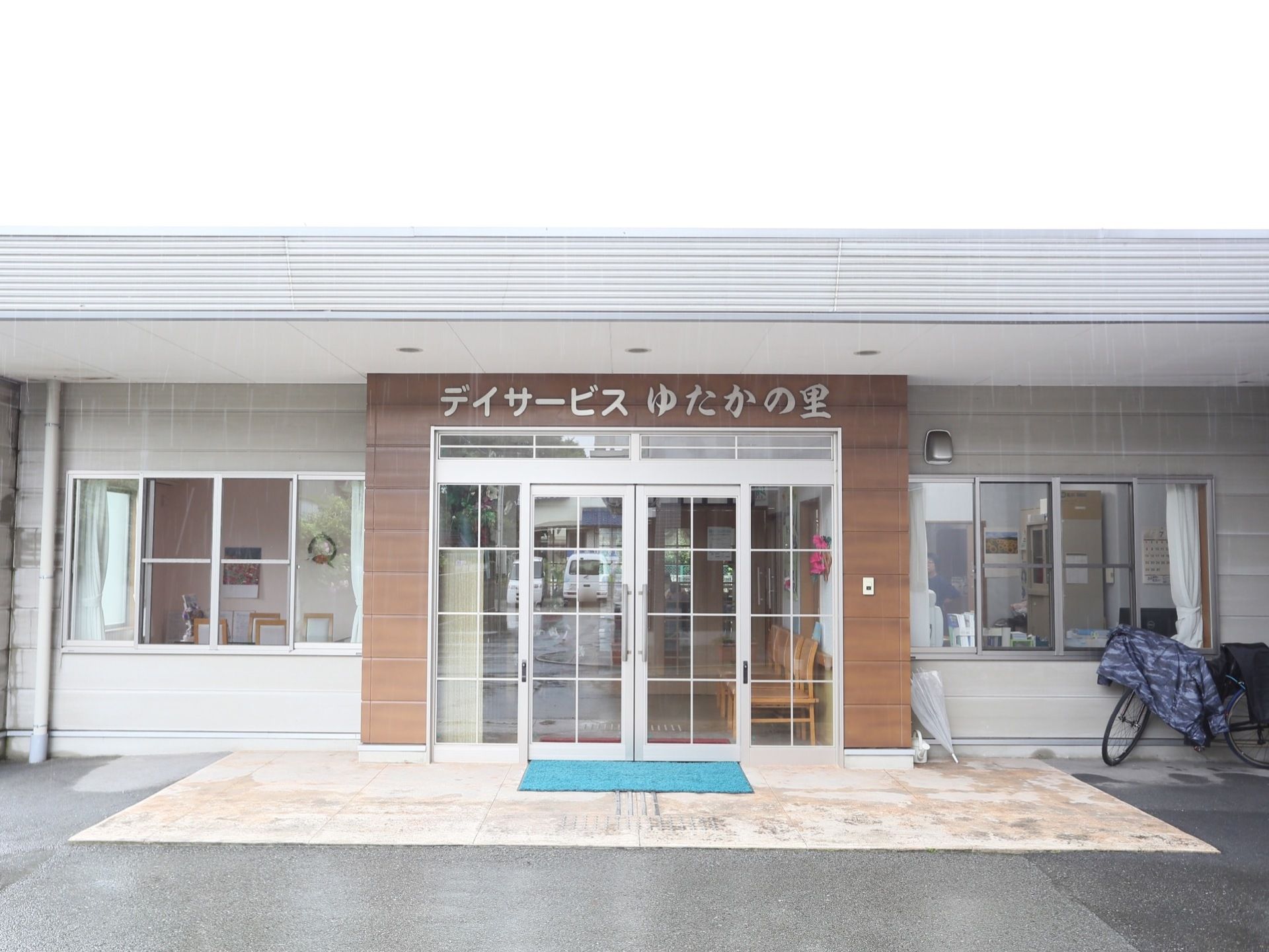 平屋建てのグレーの建物で、ガラスの大きな扉が設置されている。扉の周囲は木目調で、上部に施設名が表示されている。