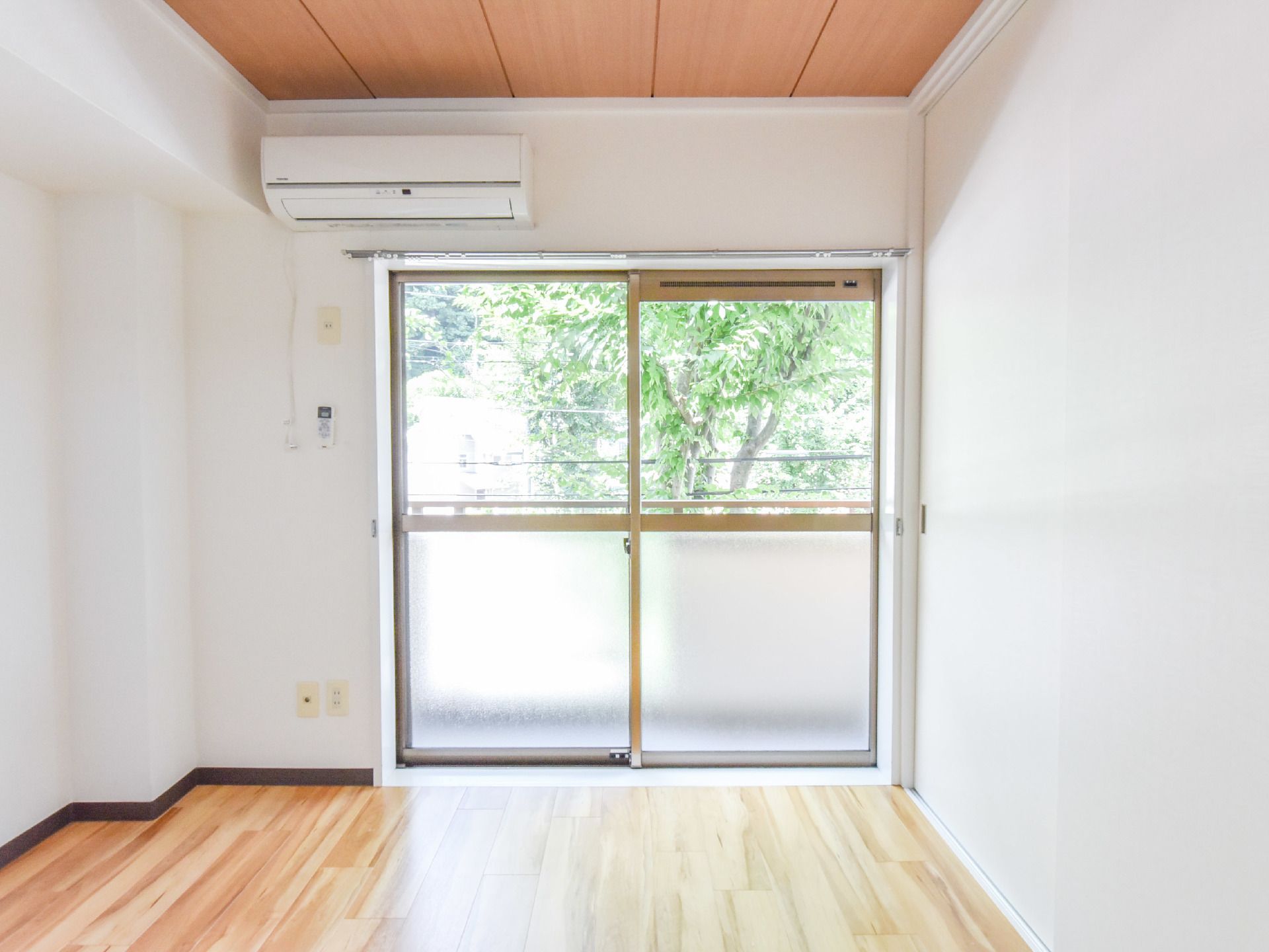 居室には日差しを取り込む大きな窓があり、外にはベランダが設けられている。上部の壁にはエアコンが設置されている。