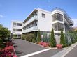 白い３階建ての建物になっていて、右側には外階段がついている。建物のまわりにはさまざまな植物が植えてあり、花壇の中にはガーデンライトがある。