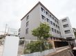 施設の看板は、白がベースで文字が緑色のすっきりとしたデザインである。建物は４階建てで、外壁の色はグレーである。