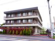 3階建ての建物には2階以上に細かい柵のベランダフェンスが設置されている。前面には生け垣があり、樹木が植えられている。