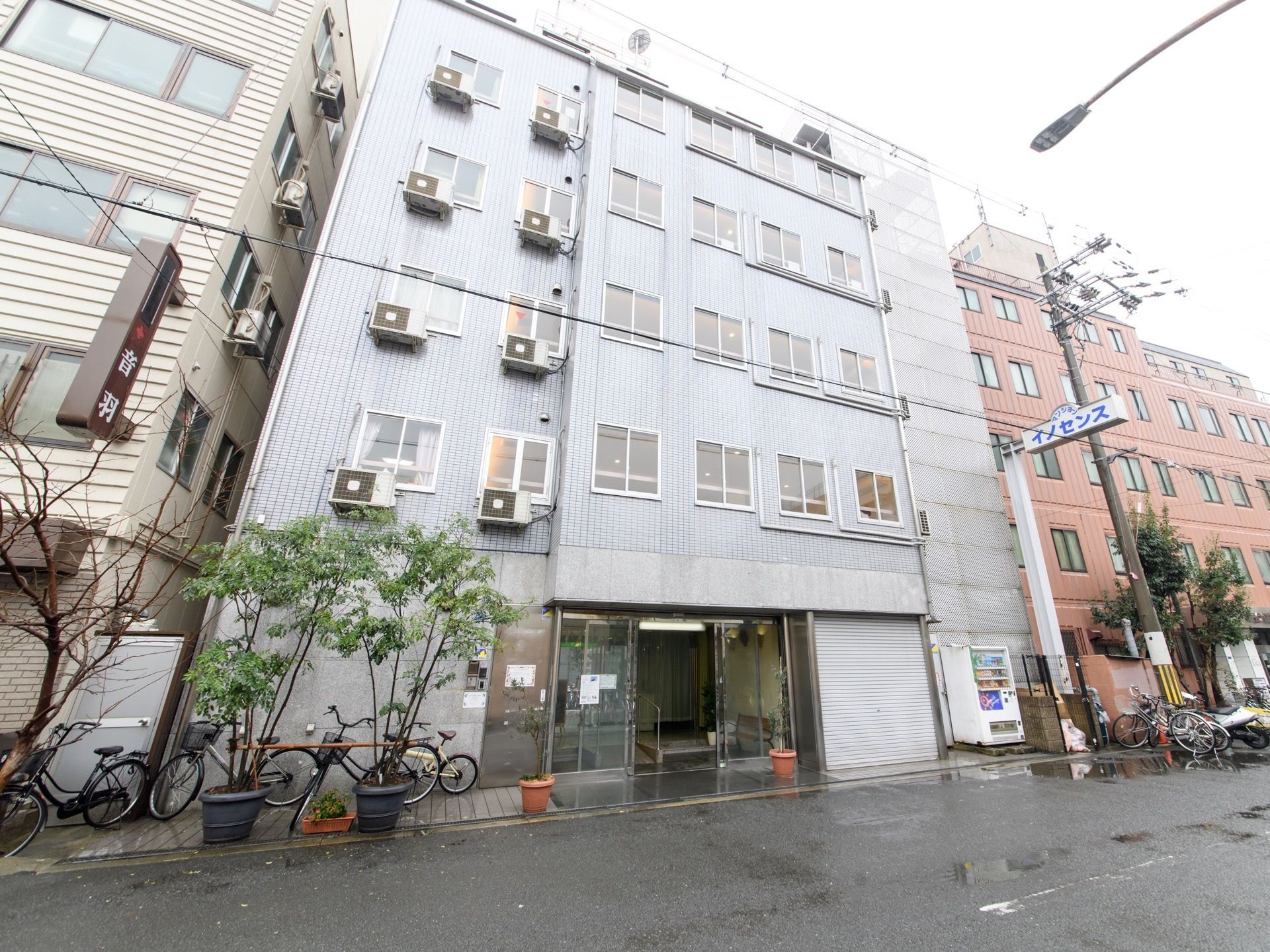 道路に面して、施設が建っている。玄関の右方向に自動販売機がある。施設名が書かれた看板が右側に掲げられている。