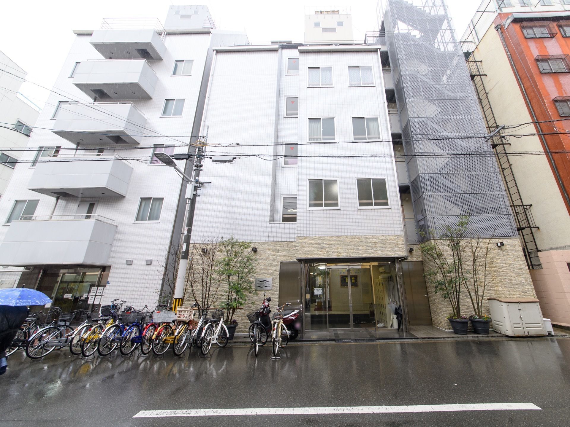 施設建物を正面から見たところ。エントランスの右側には、フェンスに囲われた非常階段が最上階まで続いている。