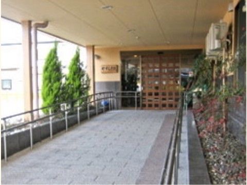 玄関への通路はスロープになっており、車椅子をご利用の方も不自由なく出入りすることができる。扉の横には木の看板がかけられている。