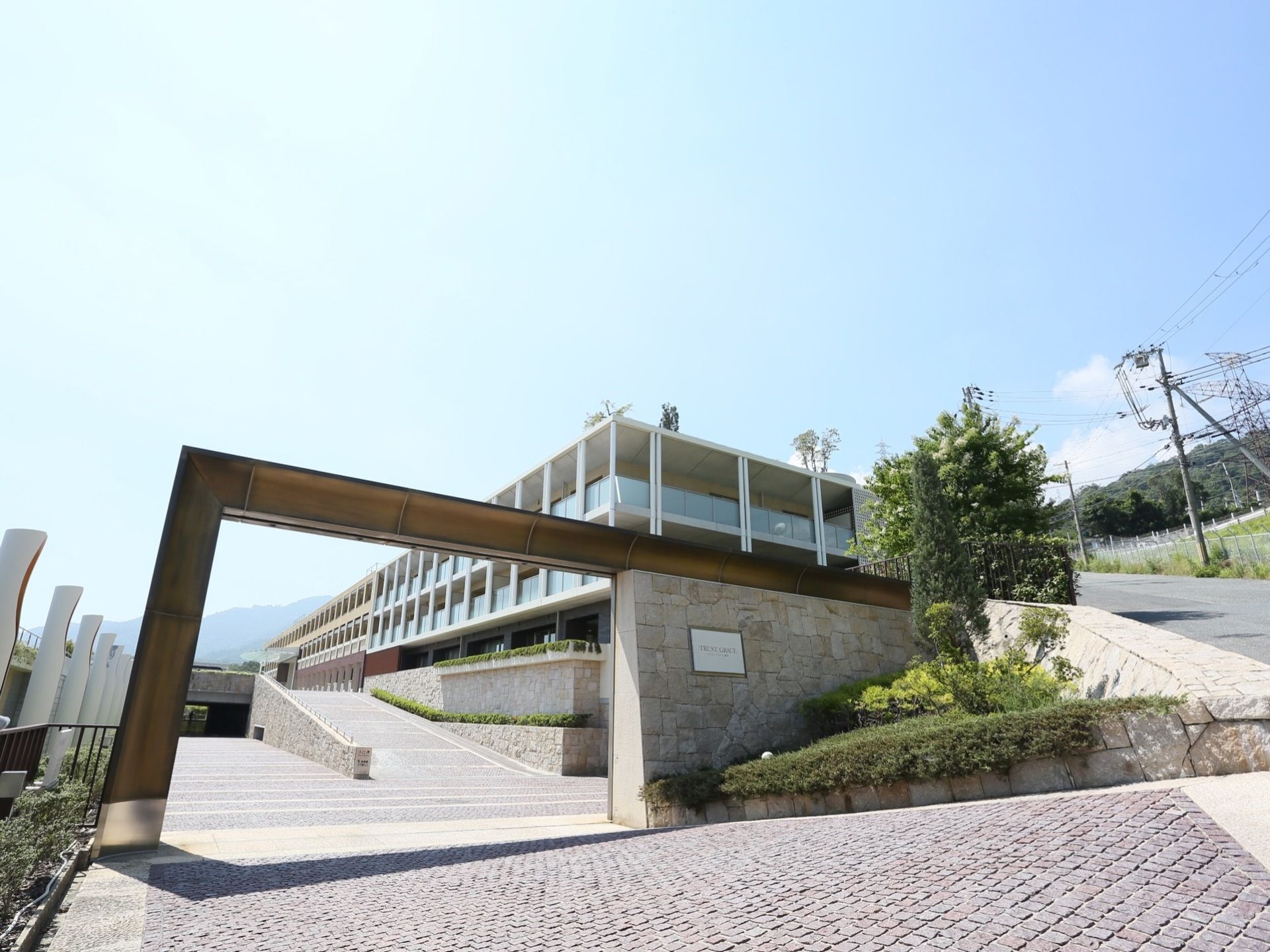 坂を下った先にゲートがあり、その奥に施設の建物が見える。敷地内へ入ると緩やかな坂が建物へと続いている。