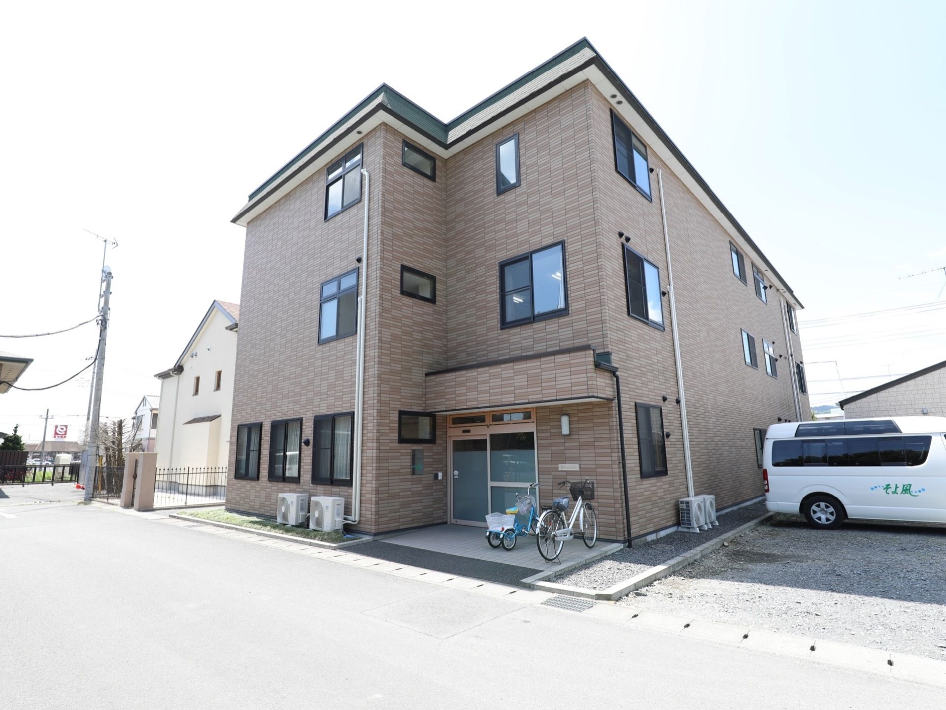 落ち着いた色味の建物。入口の前はバリアフリー構造になっている。駐車場と駐輪スペースが確保されている。