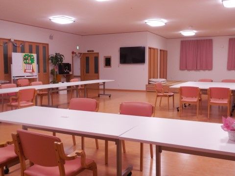 ピンク色のカーテンと椅子で統一された温かみのある食堂。壁面にはテレビやホワイトボードも設置されている。