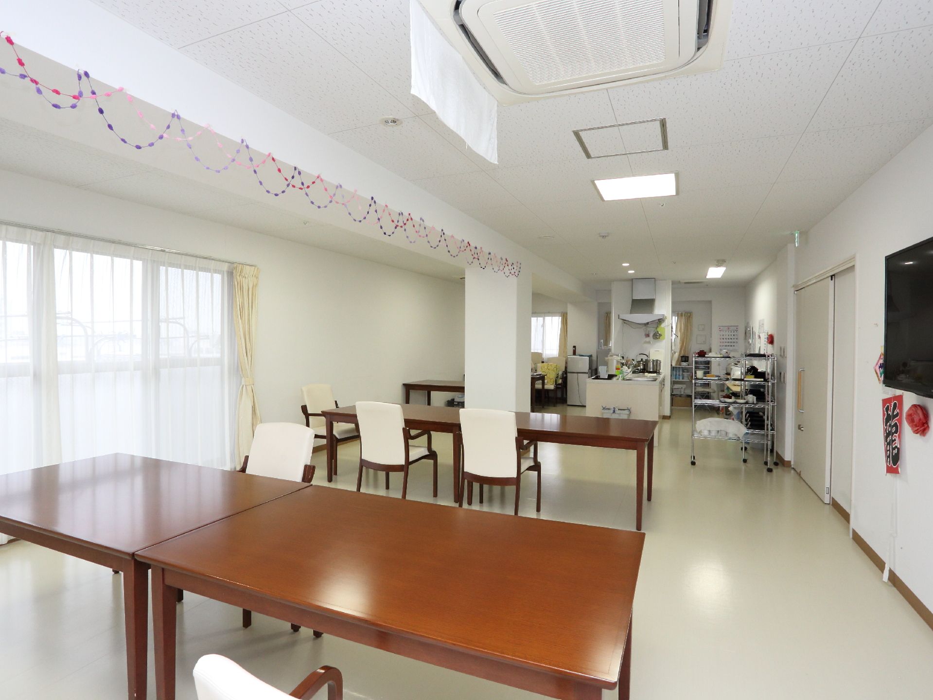 大きな窓から日の光が沢山さしこむ、明るい食堂。テーブルセットの間には余裕を持ったスペースが取られている。