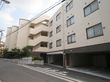 施設の前には歩道がある。一階部分に駐車場が設けてある。隣接して駐輪場がある。ブロック塀があり、植木がある。