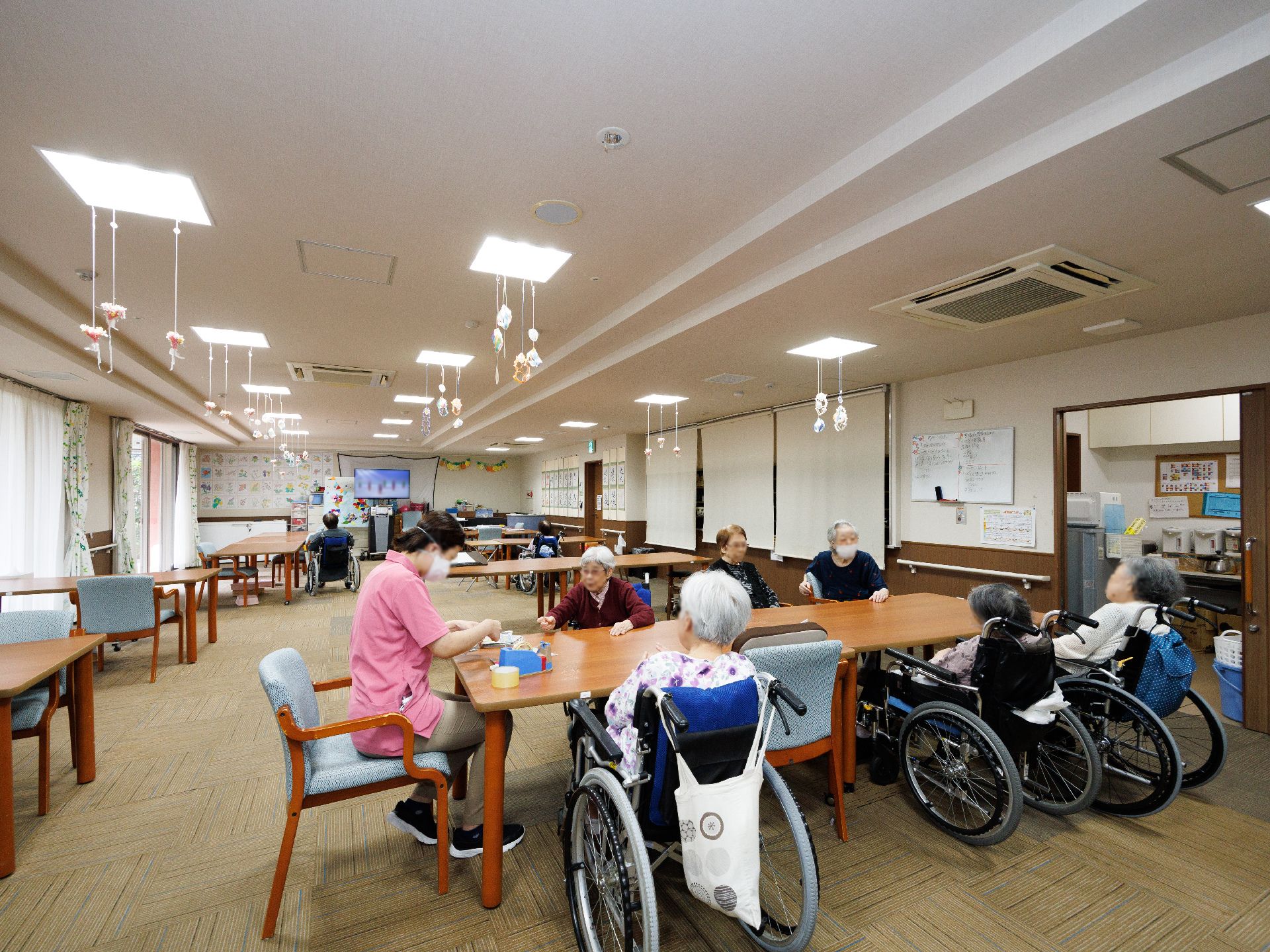 白い壁の広間に置かれた木製の机の周りに座る入居者様