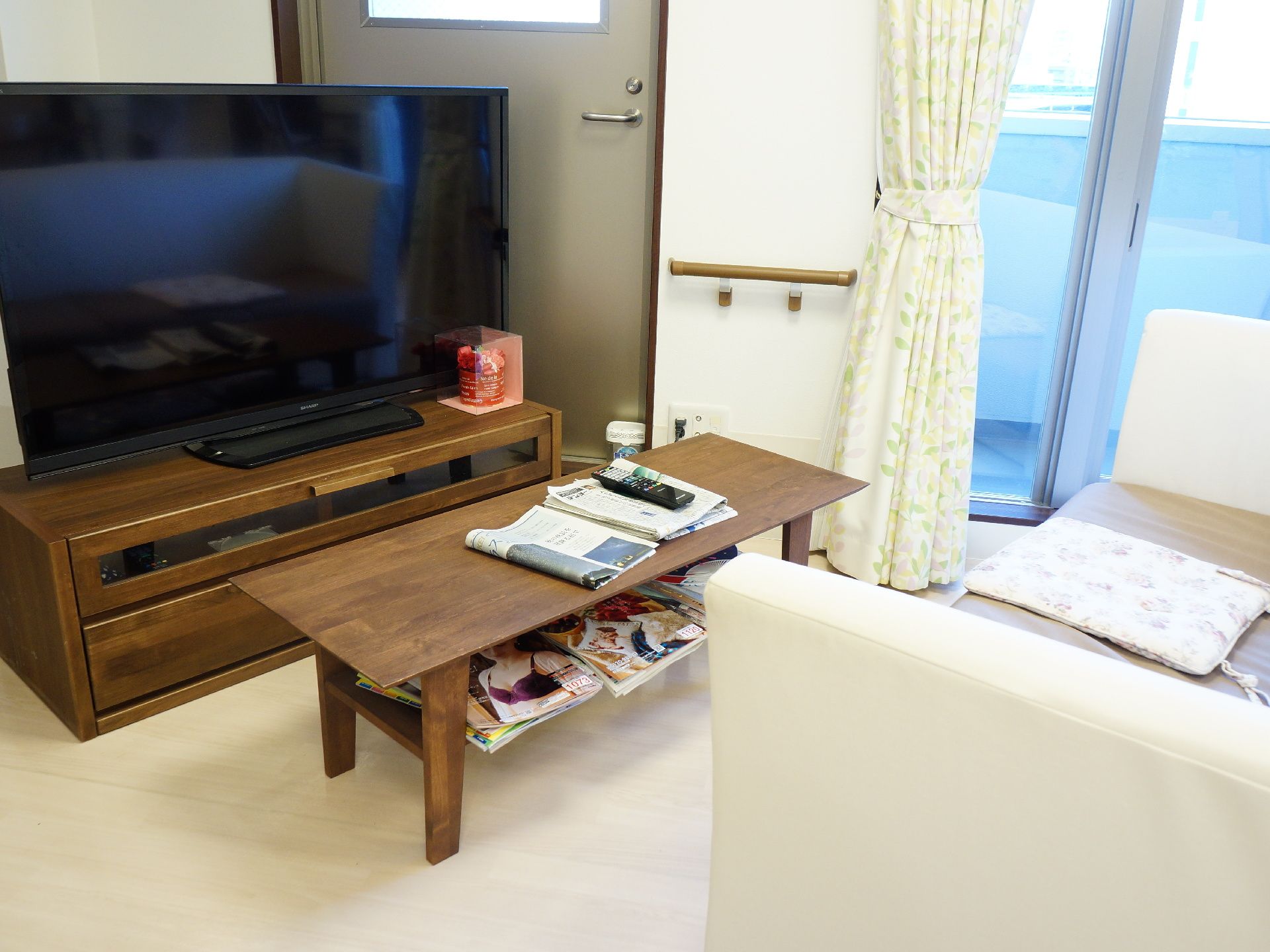 茶色のコーヒーテーブルがテレビの右手奥にある。はきだし窓がその先にある。ローボードの上にテレビが置いてある。