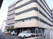 施設の一階部分に駐車場があり、車が数台停めてある。玄関の周りは、フェンスがあり、木が植栽してある。ベランダがついた建物である。