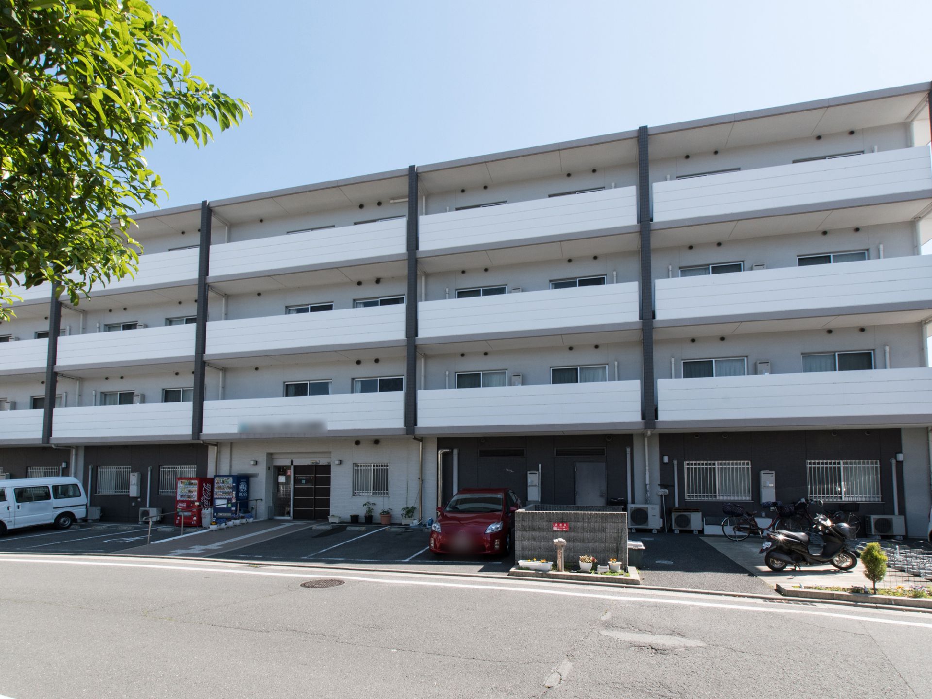 白い外壁の建物で、ベランダも白である。玄関前に、駐車場と駐輪場が設けてある。手すりのついたスロープがあるので、車椅子利用者も楽に入館できる。