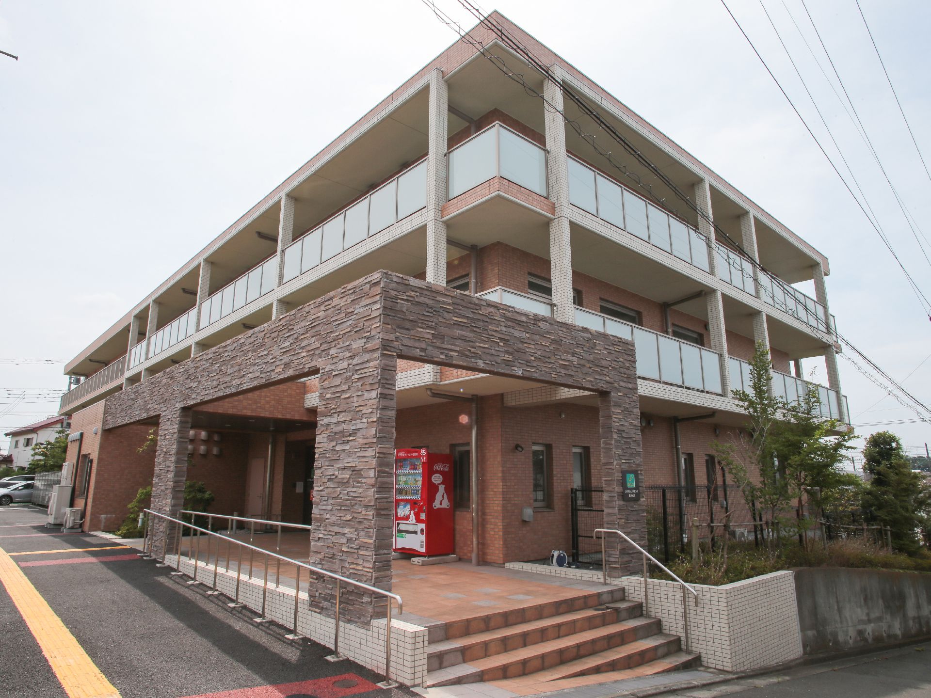 閑静な住宅街に建てらえている3階建ての施設の外観。サーモンピンクを基調としたおしゃれな雰囲気。道路からは段差のないバリアフリーとなっている。