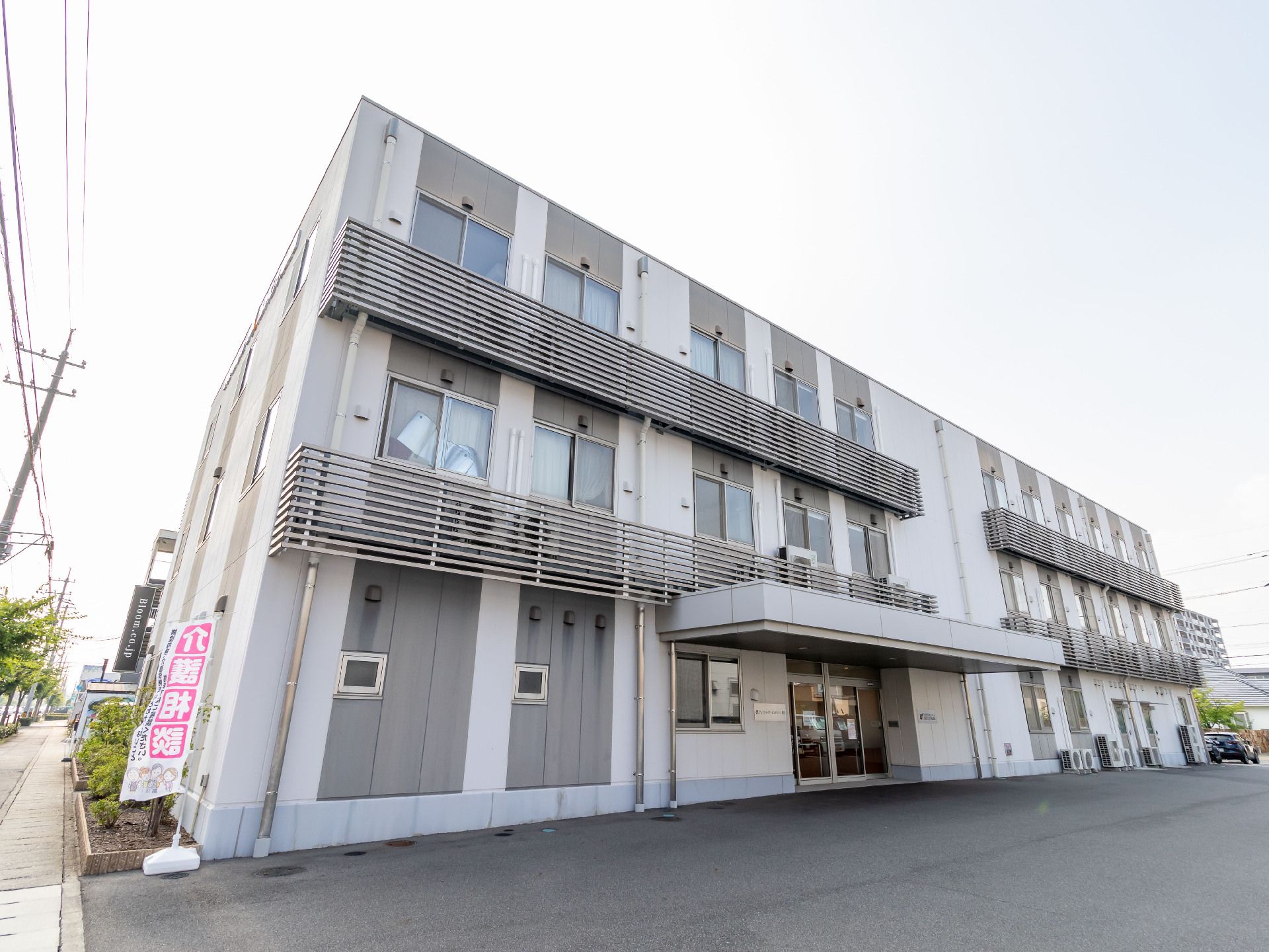 アスファルト沿いに立地した３階建てで白と灰色の外観の建物