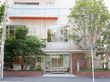 施設の出入り口の全体像である。両脇に積まれたレンガの中に緑が植えられている。外はアスファルトの道路で段差などがない。