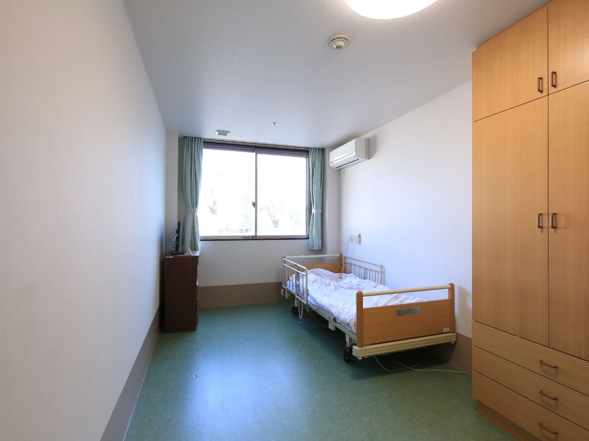 居室の床は、濃いめのグリーン。壁はホワイトにデザインされている。エアコンやベッド、クローゼットがある。