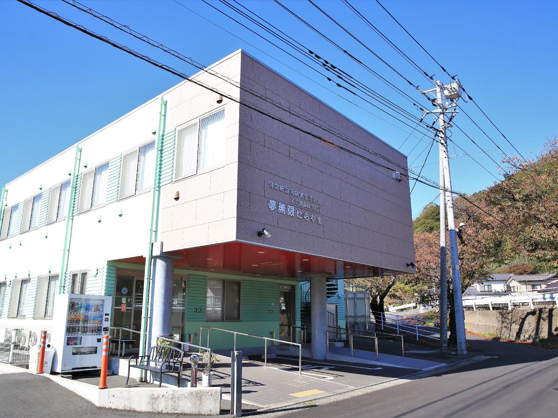 屋根が備えつけられた、エントランスである。スロープのとなりに、自動販売機が設置されている。目の前は道路である。