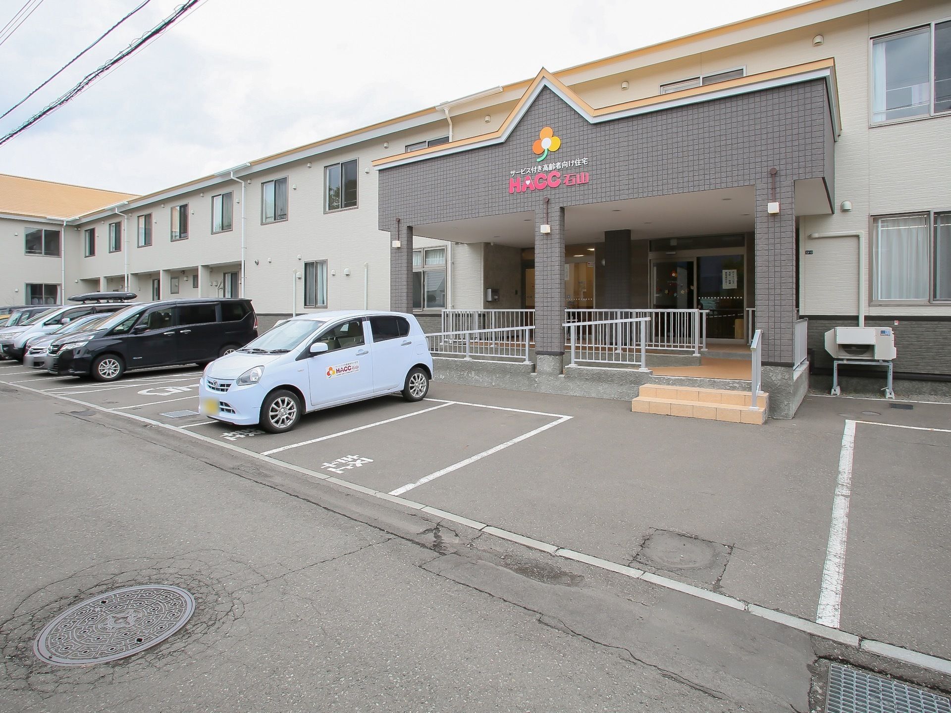 エントランスは屋根つきである。スロープには白色のフェンスを設置。車が複数台停められる、駐車場も完備されている。